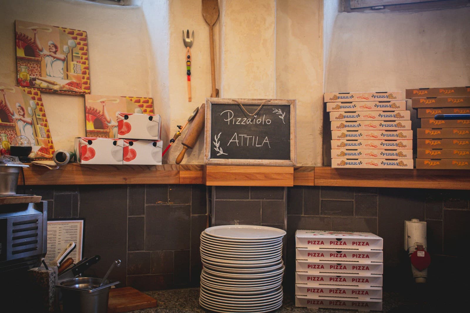 Pizzeria counter, boxes stacked, peel on the wall